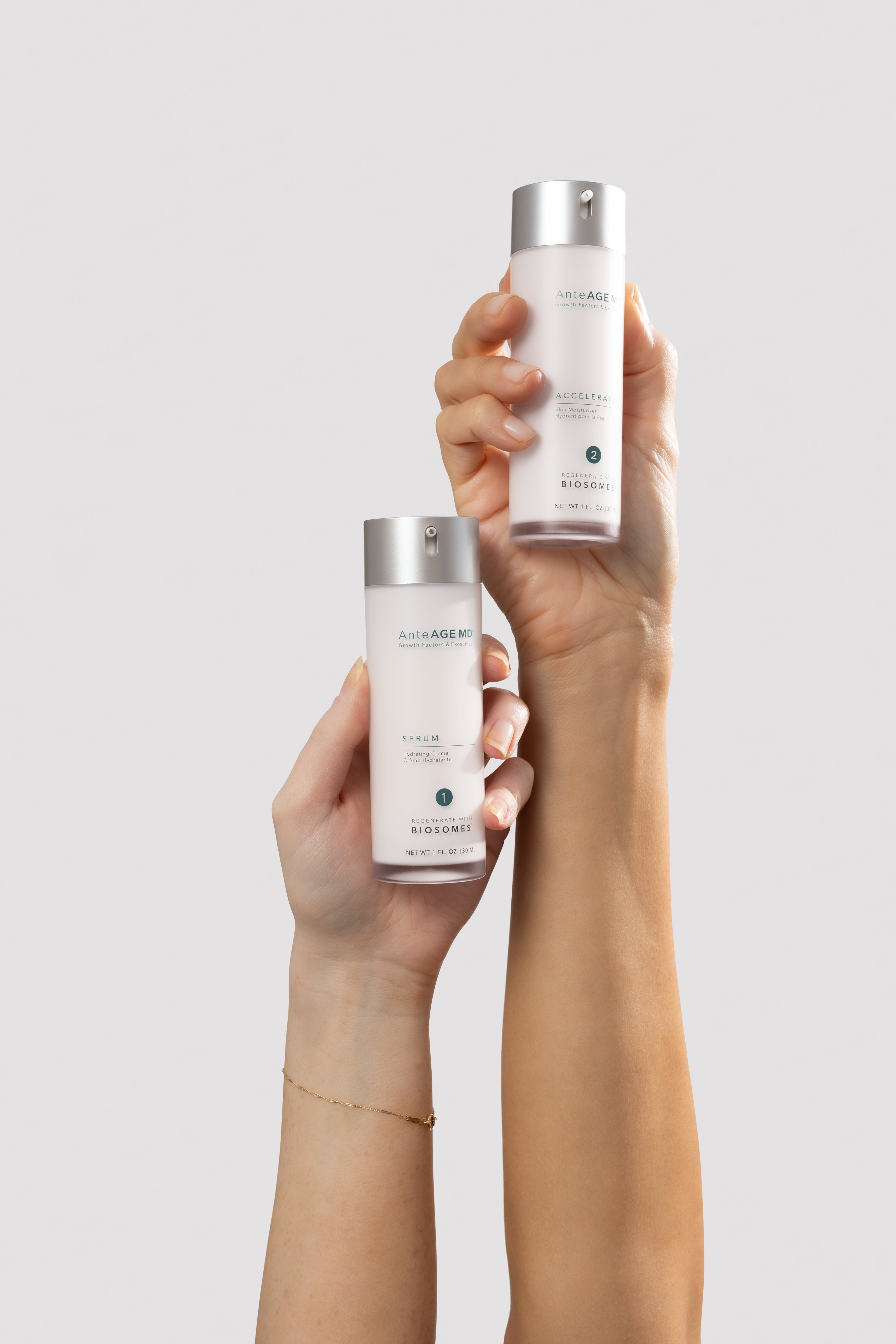 Two hands holding the AnteAGE MD Serum and Accelerator bottles raised against a light gray background